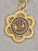 Load image into Gallery viewer, A sparkling statement piece, the Leora necklace is just the right amount of bling to add extra beauty to your outfit.  A vintage Louis Vuitton with its iconic LV symbol delicately sits in a gold floral setting, while the Figaro chain in gold shines brightly in the light.  The toggle closure adds extra brilliance to this fabulous necklace.
