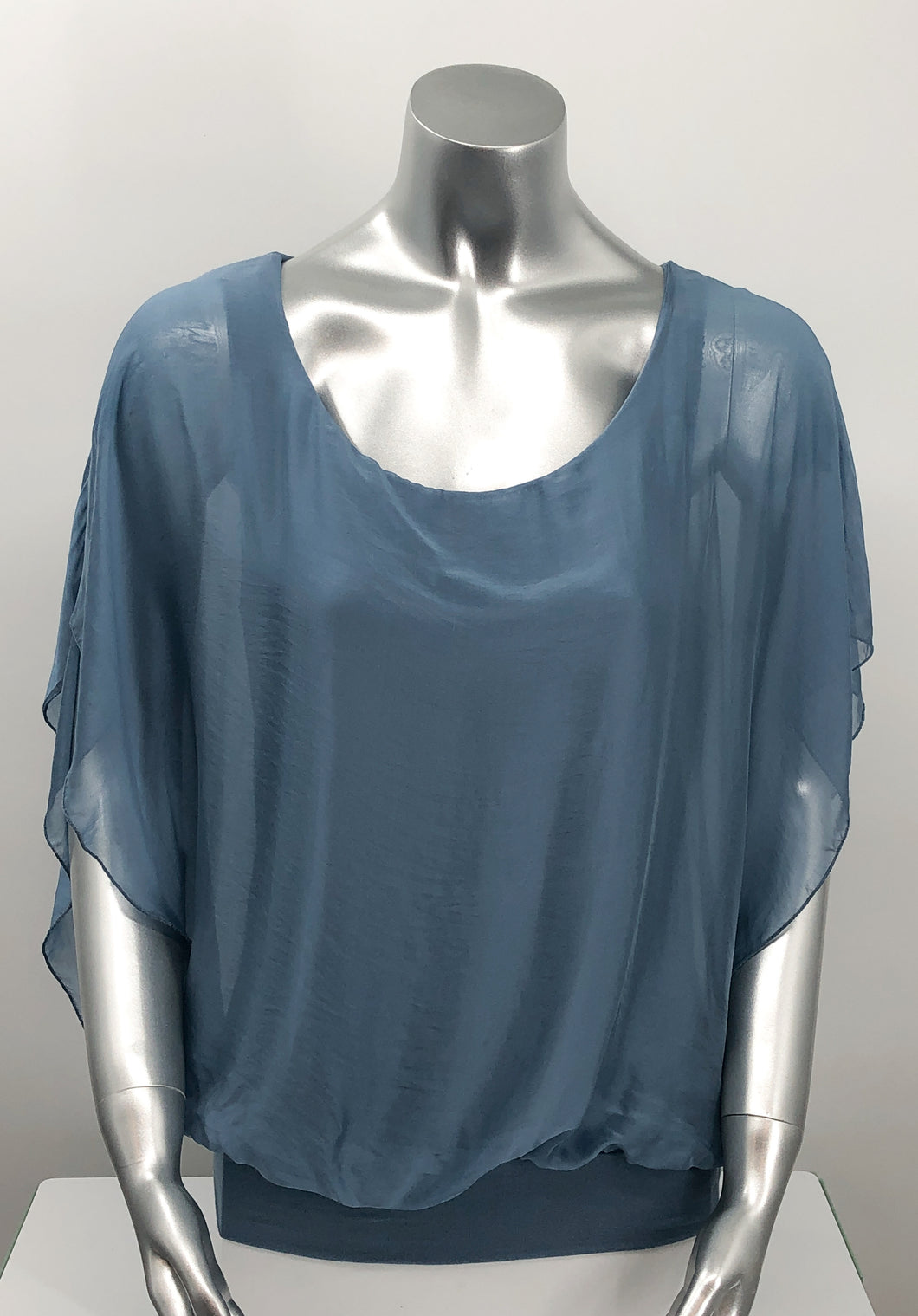 A free-flowing fabrication creates a stunning top in a slate blue color. Top is lined with a knit covered by a gorgeous silk. Bottom is banded in the same color. Create a classy and fashion forward look with our Darla by pairing it with our M Made in Italy silk bottoms.    Color- Slate blue. Knit lining slate blue. Flowy fabrication on the outside. A knit lining on the inside prevents see through.  Banded bottom.